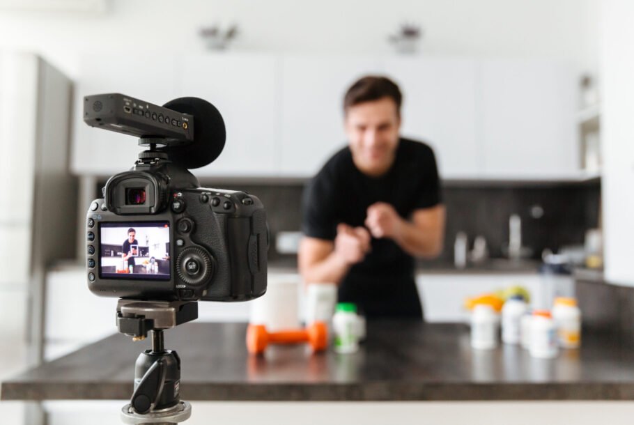 Happy young man filming his video blog episode about healthy food additives while standing at the kitchen table and pointing finger at camera